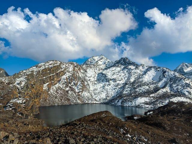 Changu Lake surrounded by snow-covered mountains under a blue sky.