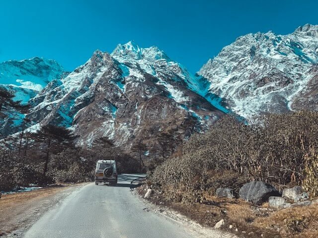Lachung with snow-covered mountains and a jeep in the foreground.